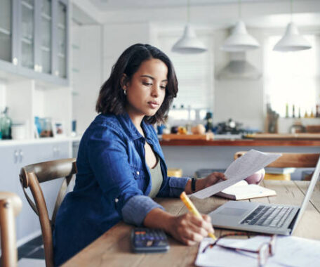 Shot of a young woman using a laptop and going through paperwork while working from home